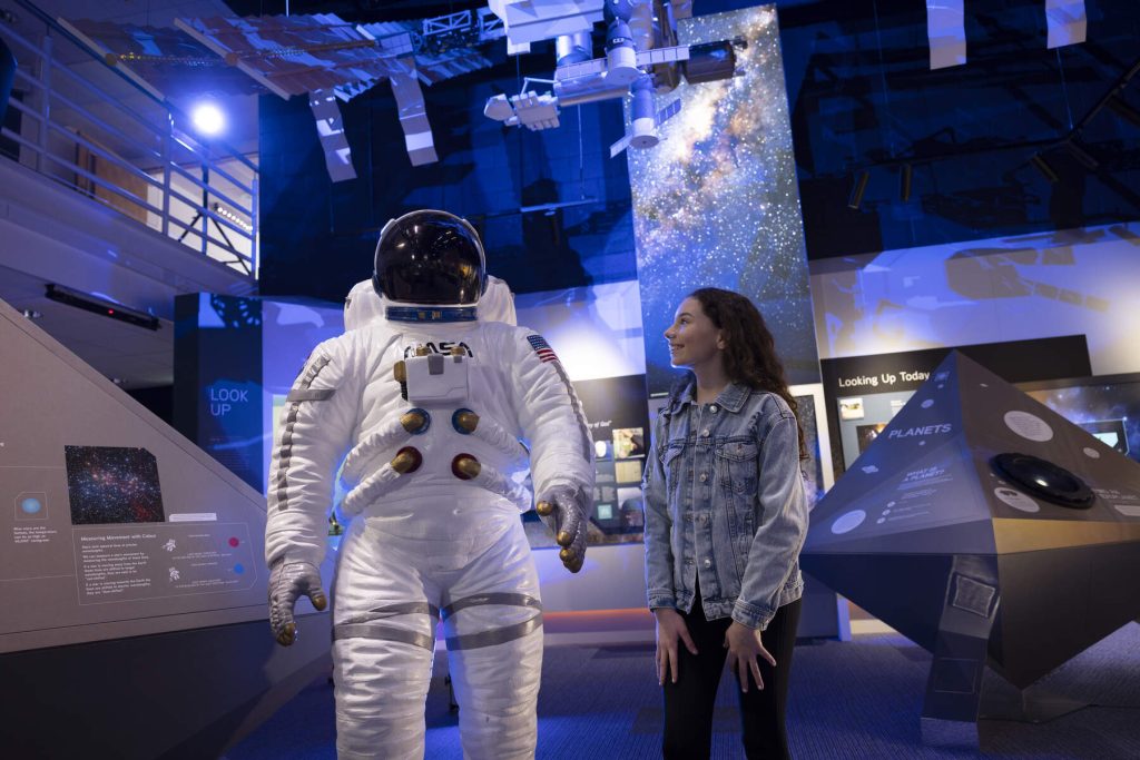 Woman stands beside astronaut costume at Armagh Planetarium