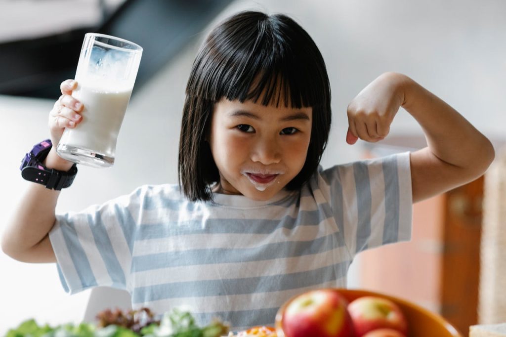 Child holding glass of milk in front of apples and other food