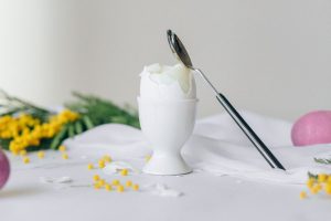 Boiled egg in a cup for breakfast with silver spoon on table with flowers