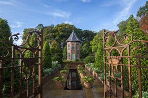 Gates open to reveal a landscaped garden with a narrow house with a green door at Antrim Castle Gardens