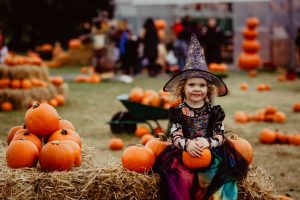 Child wearing Halloween costume sitting on hay bale with pumpkins