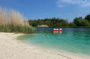 lagoon beach with white sand, green water, and three red buoys