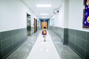 Child wearing school bag running down hallway