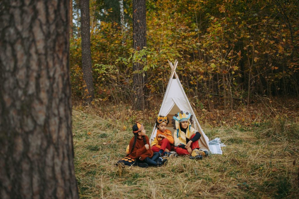 three kids in costume sitting around a teepee in a forrest