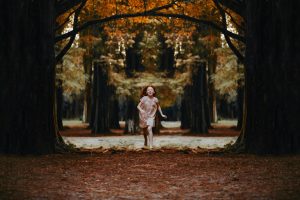 girl running barefoot through leafy forest 