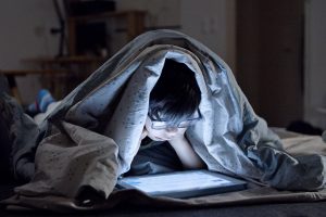 boy watching tablet with blanket covering head