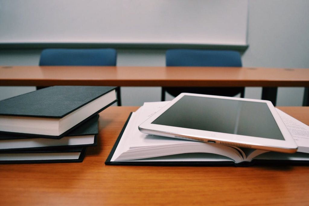 books and iPad on school table with seats and whiteboard in background